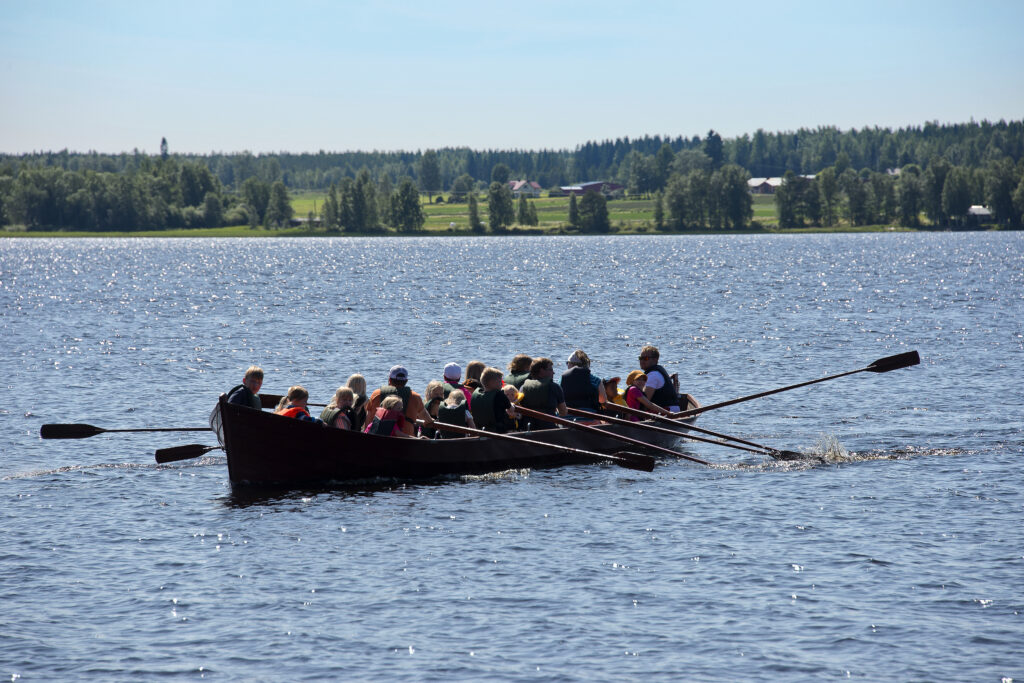 Ihmisiä soutelemassa kirkkoveneellä Kuortaneenjärvellä.
