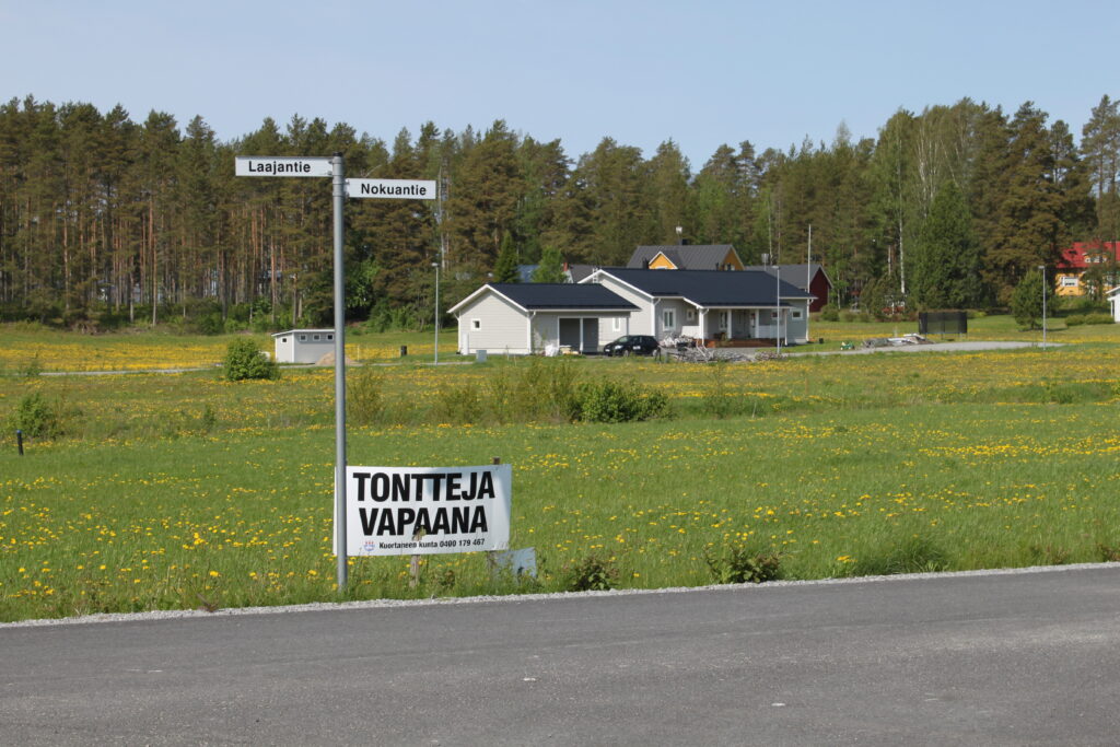 Kuva talosta aukeaman keskellä. Edessä kyltti: Tontteja vapaana.