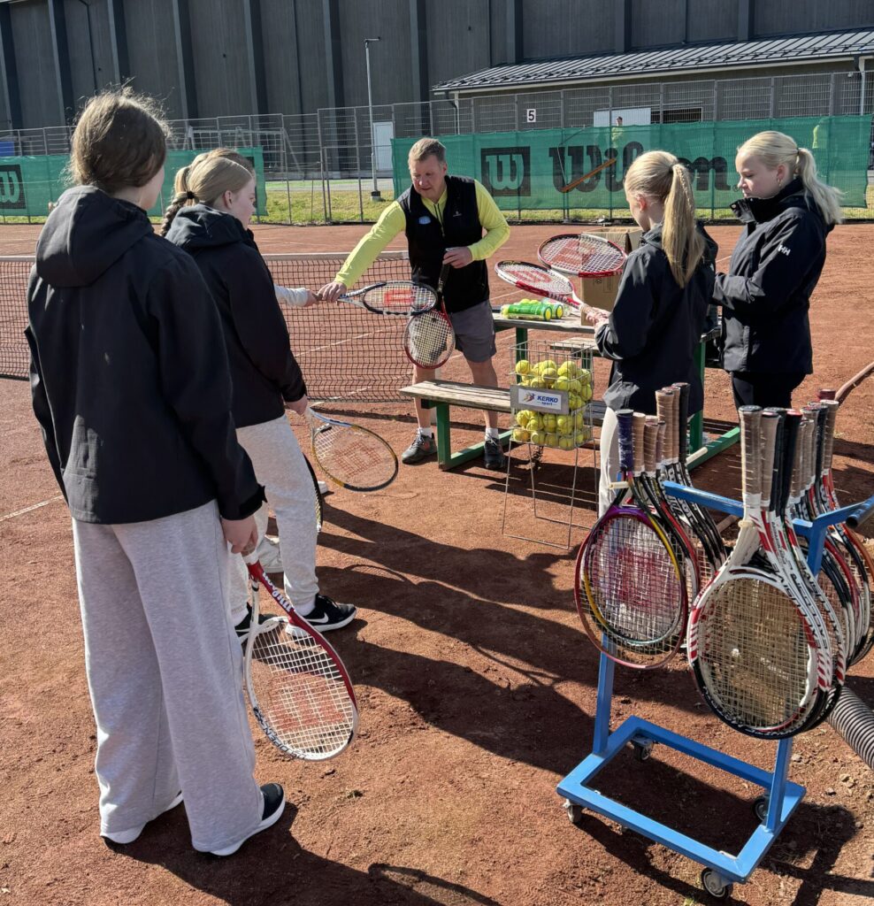 Nuoria tenniskentällä kuuntelemassa opettajaa