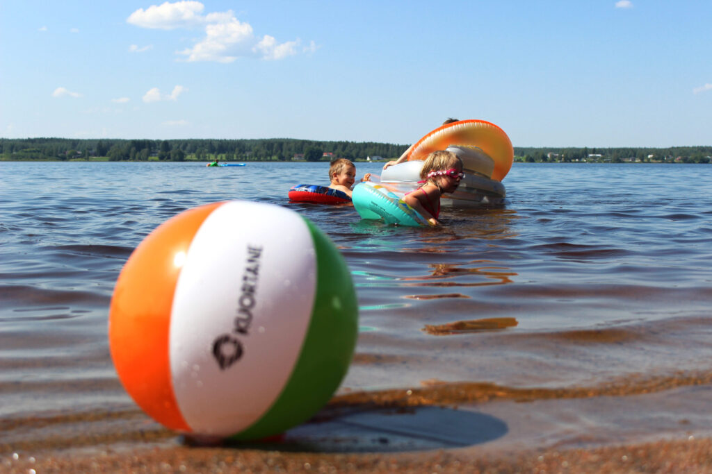 Puhallettava pallo, jossa Kuortane logo rannalla vedessä. Taustalla kaksi lasta uimassa.