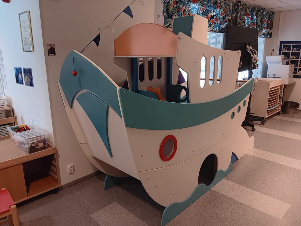 Laivan näköinen sisäleikkiteline päiväkdin sisällä.