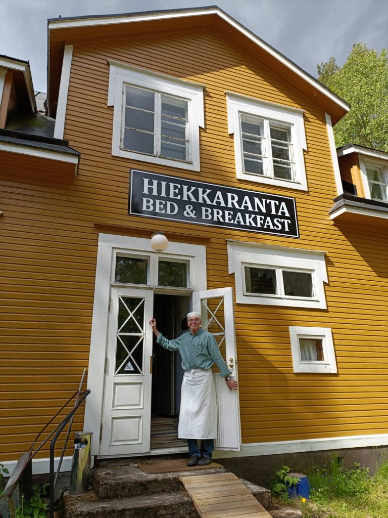 Hiekkaranta bed & breakfast ulkoovi. Omistaja seisoo oviaukossa.