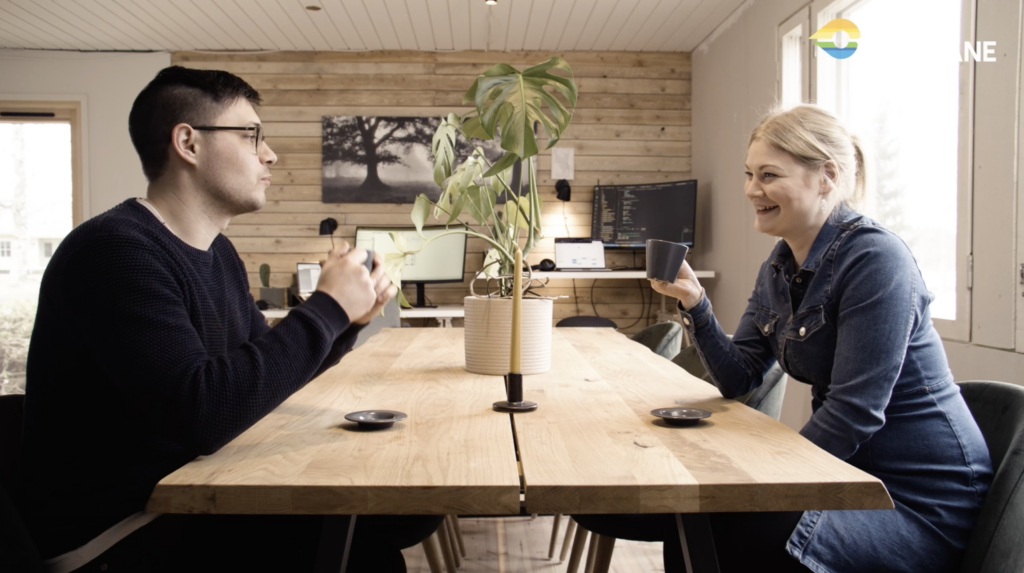 Mies ja nainen istuvat pöydän vastakkaisilla puolilla. Juovat kahvia.
