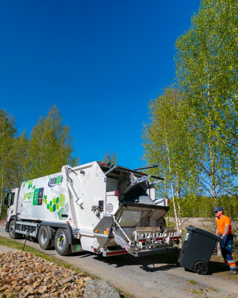 Jätteenkeräyssauto. Kuljettaja asettaa jäteastiaa keräysauton perään.