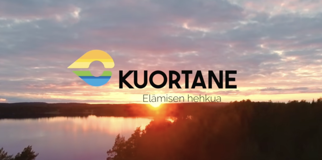Ilmakuva Kuortaneenjärvestä auringonlaskun aikaan. Kuvan päällä Kuortaneen lunnan logo.