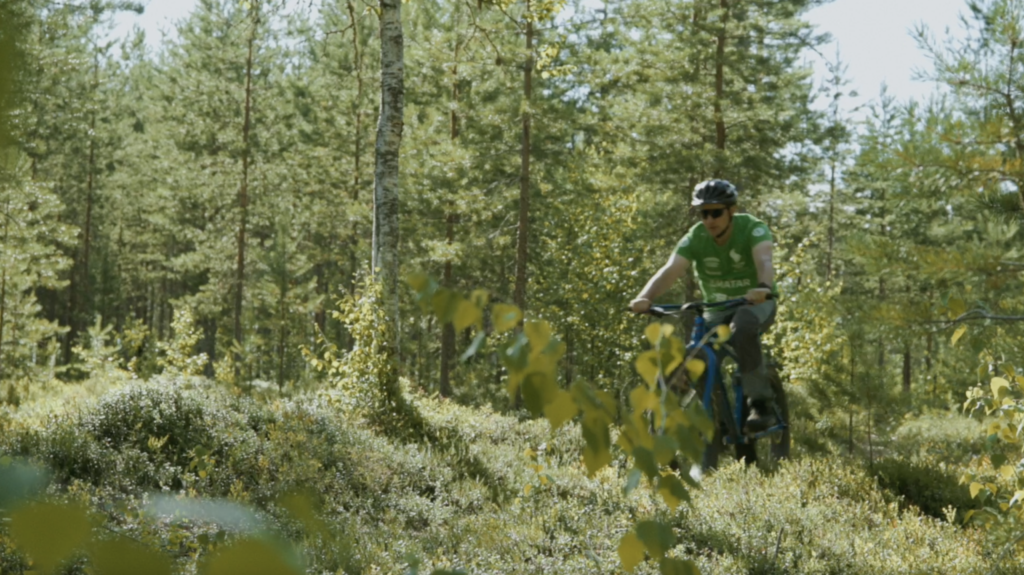 Mies vihreässä t-paidassa pyöräilee läskipyörällä kesäisessä havumetsässä.