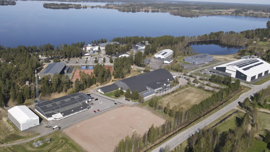 Ilmakuva Kuortaneen Urheiluopiston alueesta. Kuvassa näkyy useita eri liikuntahallirakennuksia, urheilukenttiä sekä hotelli. Taustalla laajasti aukeaa Kuortaneenjärvi.